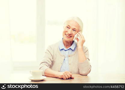 technology, communication age and people concept - happy senior woman with smartphone and coffee sitting at table and calling at home