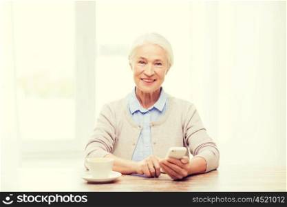 technology, communication age and people concept - happy senior woman with smartphone and coffee sitting at table and texting message at home