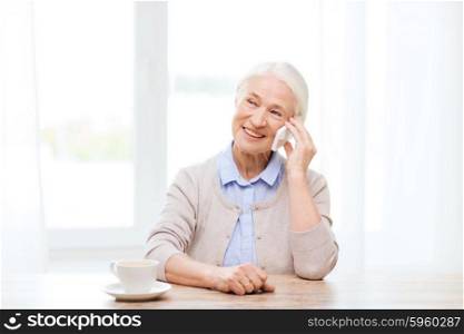 technology, communication age and people concept - happy senior woman with smartphone and coffee sitting at table and calling at home