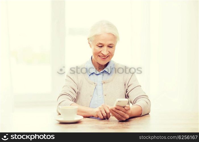 technology, communication age and people concept - happy senior woman with smartphone and coffee sitting at table and texting message at home