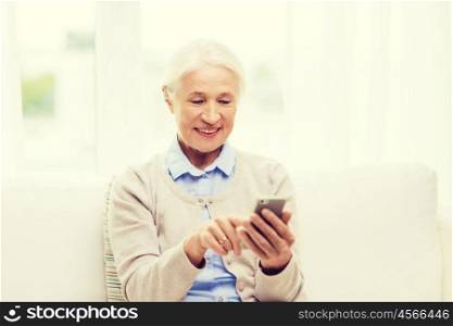 technology, communication age and people concept - happy senior woman with smartphone texting message at home