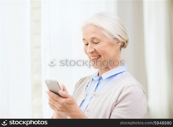 technology, communication age and people concept - happy senior woman with smartphone texting message at home