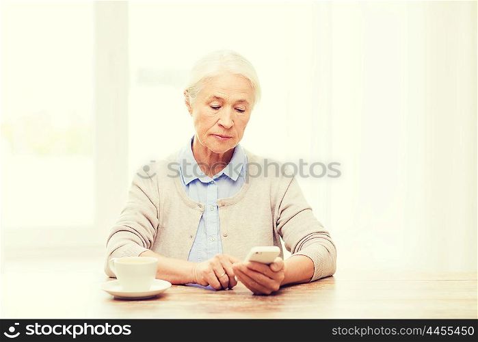 technology, communication age and people concept - senior woman with smartphone and coffee sitting at table and texting message at home