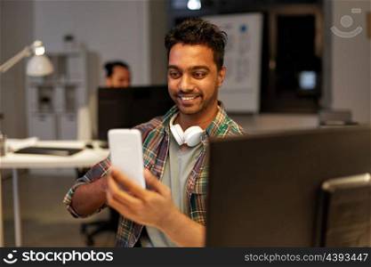 technology, communication and deadline concept - creative man with smartphone having video call at night office. man with smartphone having video call at office. man with smartphone having video call at office