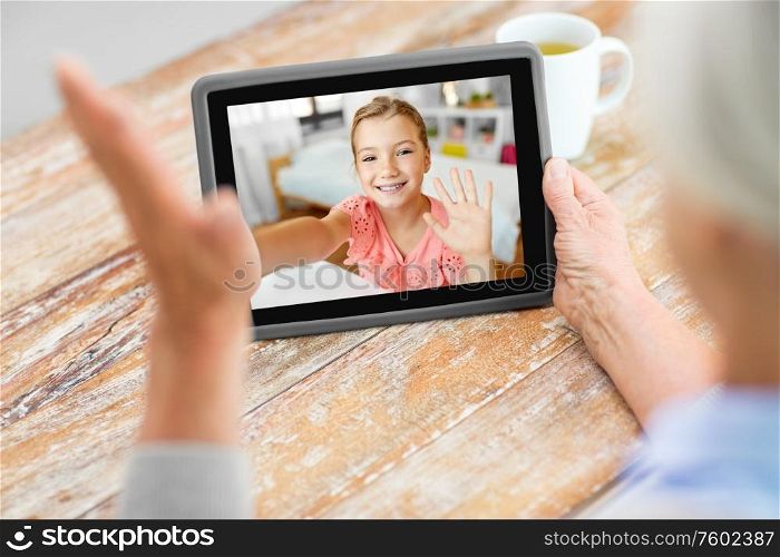 technology, communication and family concept - senior woman having video call with happy granddaughter on tablet computer at home. grandmother having video call with granddaughter