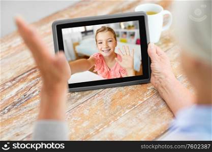 technology, communication and family concept - senior woman having video call with happy granddaughter on tablet computer at home. grandmother having video call with granddaughter