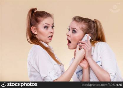 Technology communication and friendship concept. Funny teen girls using mobile phone talking, having fun, surprised emotional face expression. Girls using mobile phone talking