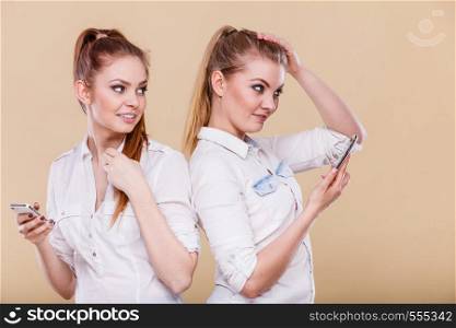Technology communication and friendship concept. Two teen girls casual style using mobile phone reading message, standing back to back. Girls using mobile phone reading message