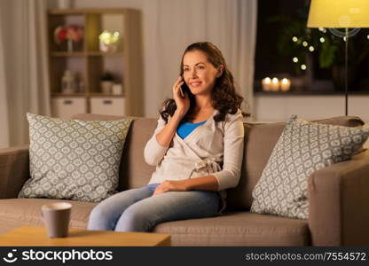 technology, communication and leisure concept - happy young woman calling on smartphone at home in evening. happy young woman calling on smartphone at home