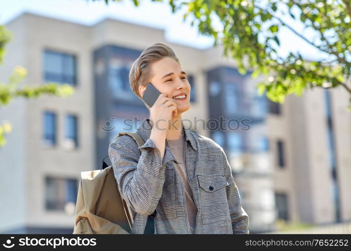 technology, communication and lifestyle concept - happy smiling young man or teenage student boy with backpack calling on smartphone on city street. teenage student boy calling on smartphone in city