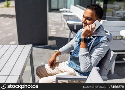 technology, communication and lifestyle concept - smiling indian man calling on smartphone at city street cafe. indian man calling on smartphone at street cafe