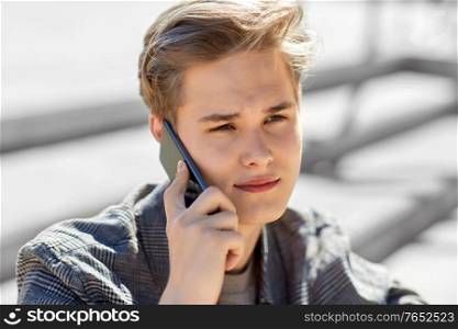 technology, communication and lifestyle concept - young man or teenage boy calling on smartphone outdoors. teenage boy calling on smartphone outdoors