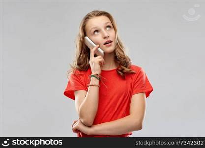 technology, communication and people concept - bored teenage girl with long hair in red t-shirt calling on smartphone over grey background. bored teenage girl calling on smartphone