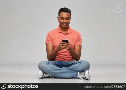technology, communication and people concept - happy indian man using smartphone over grey background. happy indian man using smartphone