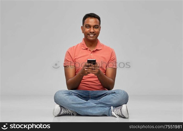technology, communication and people concept - happy indian man using smartphone over grey background. happy indian man using smartphone