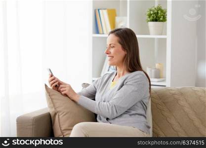 technology, communication and people concept - happy middle-aged woman messaging on smartphone at home. happy woman messaging on smartphone at home