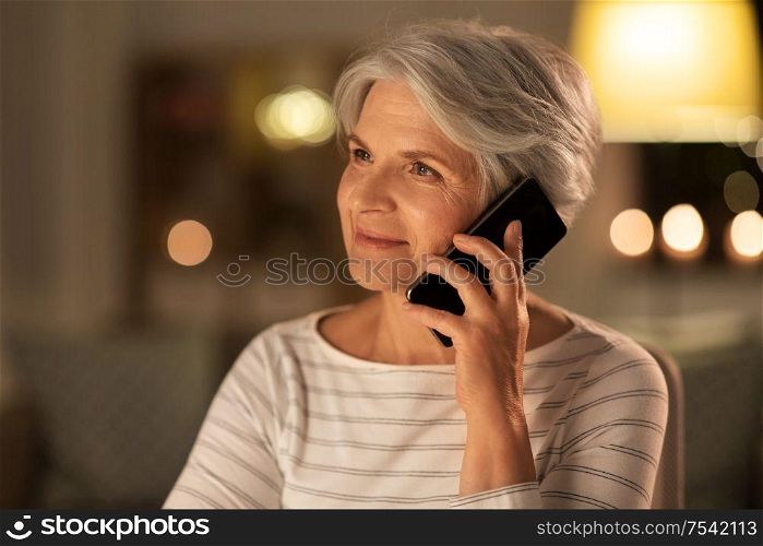 technology, communication and people concept - happy senior woman calling on smartphone at home in evening. old woman calling on smartphone at home in evening