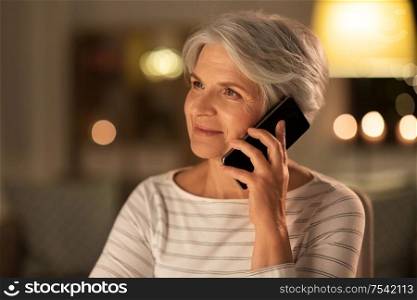 technology, communication and people concept - happy senior woman calling on smartphone at home in evening. old woman calling on smartphone at home in evening