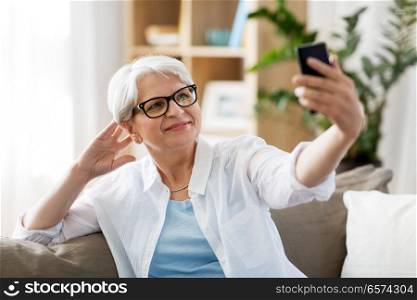 technology, communication and people concept - happy senior woman taking selfie by smartphone at home. senior woman taking selfie by smartphone at home