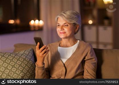 technology, communication and people concept - happy senior woman with smartphone at home in evening. happy senior woman with smartphone at home
