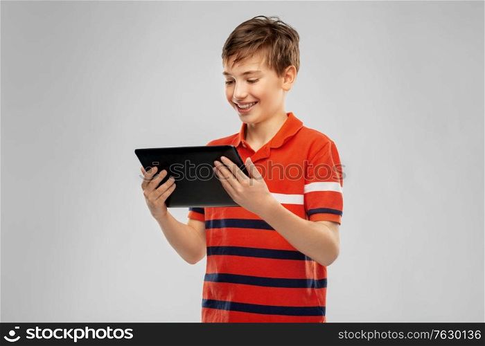 technology, communication and people concept - happy smiling boy in red polo t-shirt using tablet pc computer over grey background. happy smiling boy using tablet computer