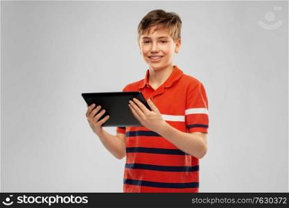 technology, communication and people concept - happy smiling boy in red polo t-shirt using tablet pc computer over grey background. happy smiling boy using tablet computer