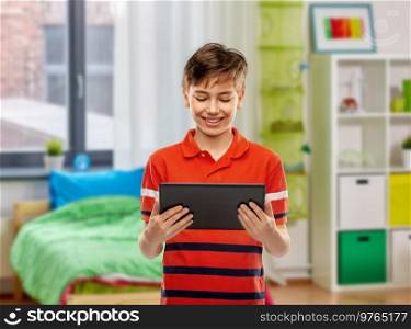 technology, communication and people concept - happy smiling boy in red polo t-shirt using tablet pc computer over home room background. happy smiling boy using tablet computer at home