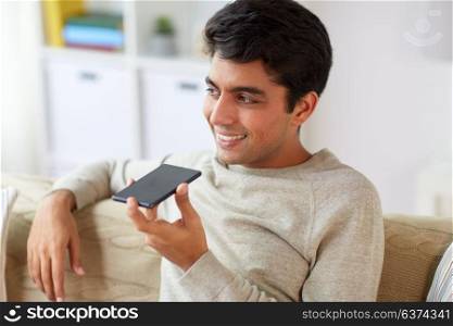 technology, communication and people concept - happy smiling man using voice command recorder on smartphone at home. man using voice command recorder on smartphone