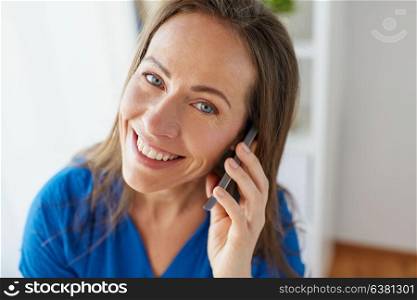 technology, communication and people concept - happy smiling middle-aged woman calling on smartphone at office or home. woman calling on smartphone at office or home