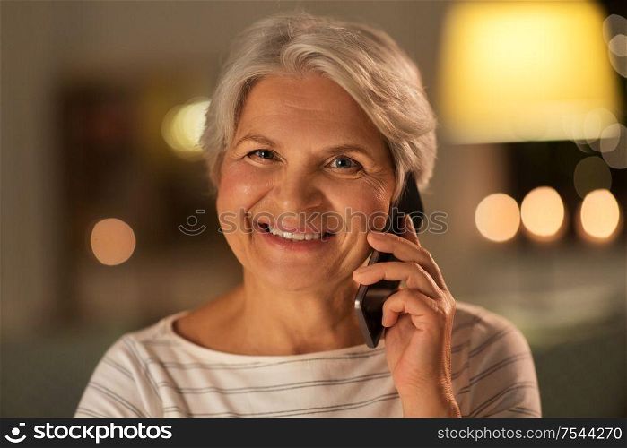 technology, communication and people concept - happy smiling senior woman calling on smartphone at home in evening. old woman calling on smartphone at home in evening