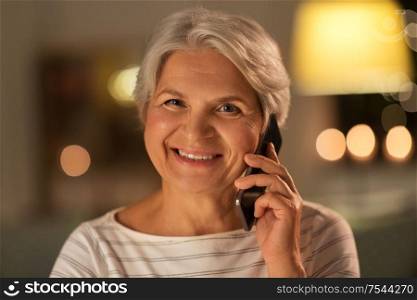 technology, communication and people concept - happy smiling senior woman calling on smartphone at home in evening. old woman calling on smartphone at home in evening