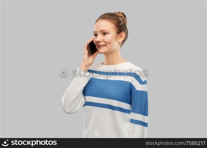 technology, communication and people concept - happy smiling teenage girl in pullover calling on smartphone over grey background. happy smiling teenage girl calling on smartphone