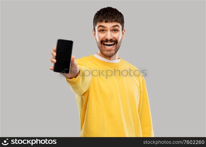 technology, communication and people concept - happy smiling young man showing smartphone over grey background. happy smiling young man showing smartphone
