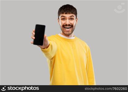 technology, communication and people concept - happy smiling young man showing smartphone over grey background. happy smiling young man showing smartphone