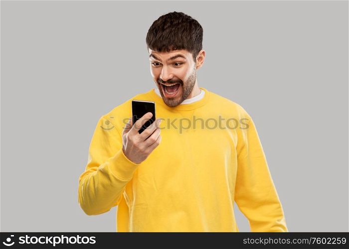 technology, communication and people concept - happy smiling young man with smartphone over grey background. happy smiling young man with smartphone