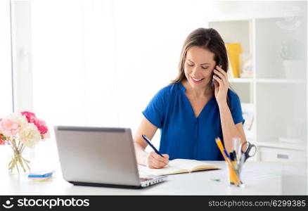 technology, communication and people concept - happy woman calling on smartphone and writing to notebook at office or home. woman with notepad calling on smartphone at office