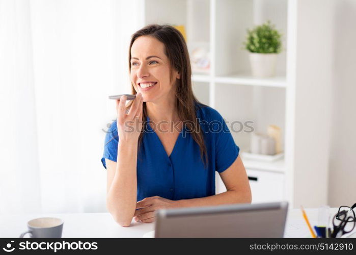 technology, communication and people concept - happy woman using voice command recorder on smartphone at office. woman using voice recorder on smartphone at office