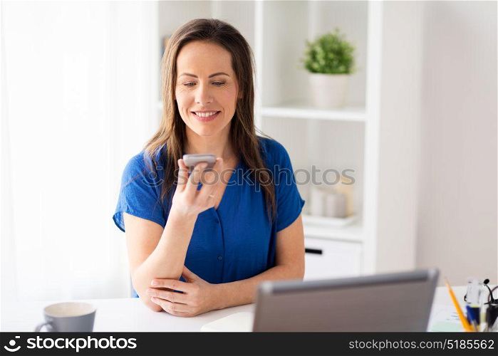 technology, communication and people concept - happy woman using voice command recorder on smartphone at office. woman using voice recorder on smartphone at office