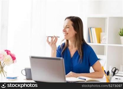 technology, communication and people concept - happy woman using voice command recorder on smartphone at office. woman using voice recorder on smartphone at office