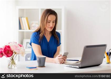 technology, communication and people concept - happy woman with smartphone and laptop computer at office. woman with smartphone and laptop at office