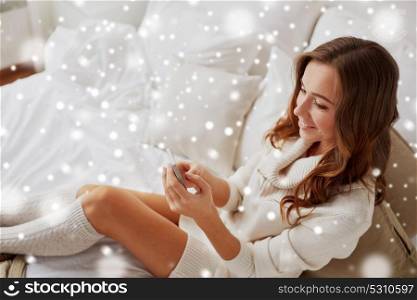 technology, communication and people concept - happy young woman in bed and texting on smartphone at home bedroom with snow. happy young woman with smartphone in bed at home