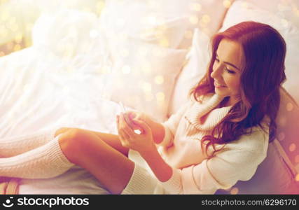 technology, communication and people concept - happy young woman lying in bed and texting on smartphone at home bedroom. happy young woman with smartphone in bed at home