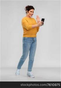 technology, communication and people concept - happy young woman with smartphone having video call over grey background. happy young woman having video call on smartphone