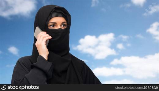 technology, communication and people concept - muslim woman in hijab calling on smartphone over blue sky and clouds background. muslim woman in hijab over white background