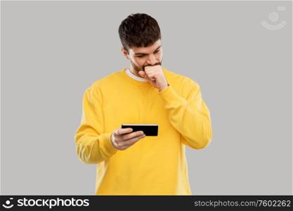 technology, communication and people concept - puzzled young man with smartphone over grey background. puzzled young man with smartphone