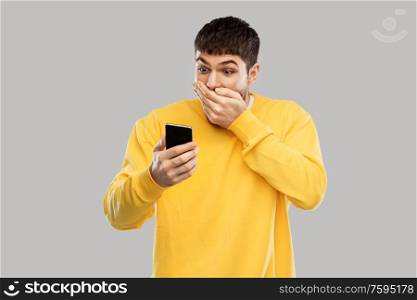 technology, communication and people concept - shocked young man with smartphone over grey background. shocked young man with smartphone