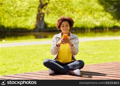 technology, communication and people concept - smiling african american young woman or teenage girl messaging on smartphone at summer park