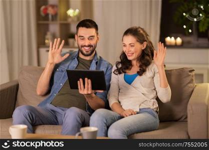 technology, communication and people concept - smiling happy couple with tablet pc computer having video call at home in evening. couple with tablet pc having video call at home