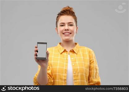 technology, communication and people concept - smiling red haired teenage girl in checkered shirt showing blank screen of smartphone over grey background. smiling red haired teenage girl showing smartphone