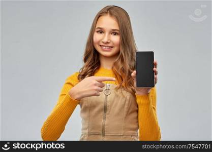 technology, communication and people concept - smiling teenage girl showing blank screen of smartphone over grey background. smiling teenage girl showing smartphone